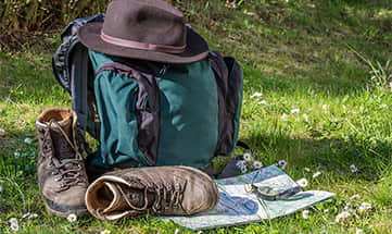 Wanderstiefel, Wanderkarte, Hut und Rucksack auf einer Wiese